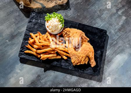 Knusprig gebratenes Spring Chicken (halb) mit pommes Frites und Mayo-Dip in einem schwarzen Gericht Draufsicht auf dunklem Hintergrund Fast Food Stockfoto