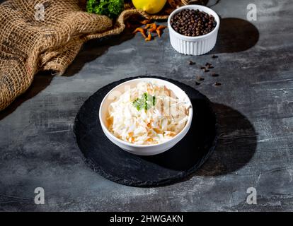 Frisch zubereiteter Krautsalat, zerkleinert Weißkohl, Mayonnaise und geriebene Karotte in der Schüssel, Seitenansicht auf dunklem Hintergrund Stockfoto