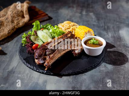 Rosmarin Lamp Chop mit Chilisauce, Salat, Nudeln, Mais in einem Gericht Draufsicht auf dunklem Hintergrund Stockfoto