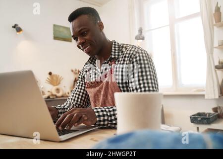 Fröhlicher Töpfer, der im Studio am Laptop arbeitet Stockfoto