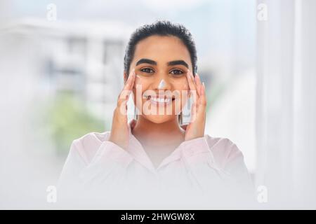 Ich liebe es, meine Haut zu pflegen, weil es sich auszahlt. Kurzer Schuss einer schönen jungen Frau, die ihr Gesicht mit einer Feuchtigkeitscreme versorgt. Stockfoto