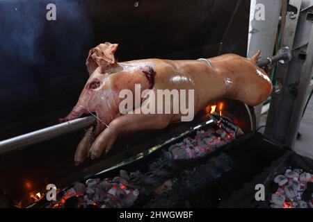 Schwein wird langsam vom Grill auf Spit in traditioneller Art, mit Holzkohle, fettes gebratenes Fleisch gekocht Stockfoto