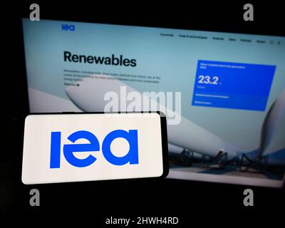 Person, die das Smartphone mit dem Logo der Organisation International Energy Agency (IEA) auf dem Bildschirm vor der Website hält. Konzentrieren Sie sich auf die Telefonanzeige. Stockfoto