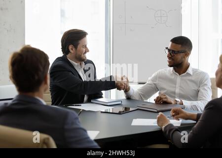 Glückliche, vielfältige Partner, die sich im modernen Büro die Hände schütteln. Stockfoto