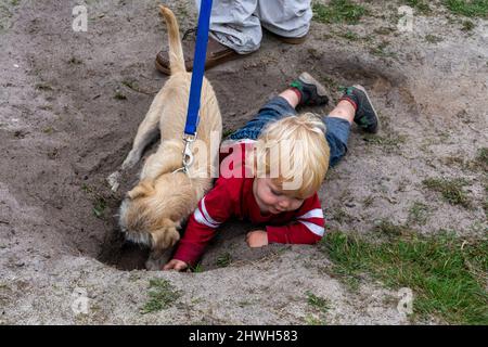 Kleine Kinder spielen in den Schmutz mit einem Hund, ein Loch gegraben. Konzept der Kinder beim Spielen in der freien Natur - gesunde Kindheit - natürliche Immunität Stockfoto