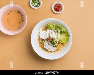 vietnamesische Küche Fischnudel in Scheiben geschnitten in einer Schüssel mit Suppe, Chilisauce und Frühlingszwiebeln Draufsicht auf Holztisch Stockfoto