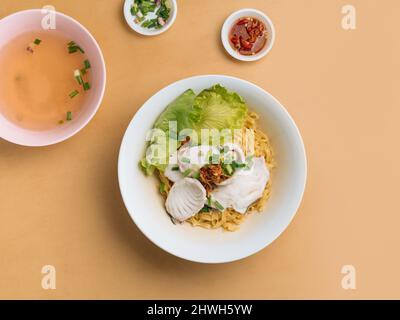 vietnamesische Küche Fischnudel in Scheiben geschnitten in einer Schüssel mit Suppe, Chilisauce und Frühlingszwiebeln Draufsicht auf Holztisch Stockfoto