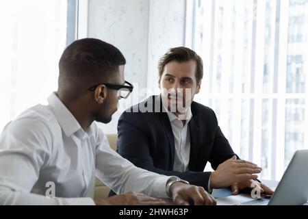 Fokussierte, multirassische Partner entwickeln Online-Strategie mit Laptop. Stockfoto