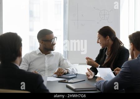 Glückliche junge, vielfältige Kollegen diskutieren im Büro über Arbeitsfragen. Stockfoto