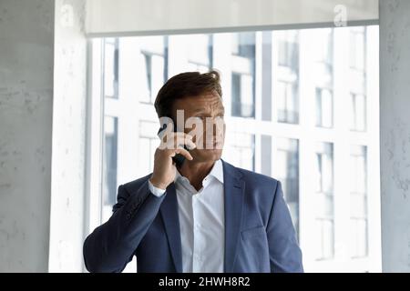 Fokussierter, ernsthafter Geschäftsmann mittleren Alters, der ein Telefongespräch führt. Stockfoto