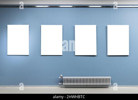 In einer Ausstellungshalle hängen vier weiße vertikale Poster an der blauen Wand. Leerer Innenraum, Vorderansicht, Hintergrundbild Stockfoto