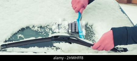 Hand mit Pinsel und entfernen Schnee von Auto und Windschutzscheibe. Winterprobleme beim Transport Stockfoto