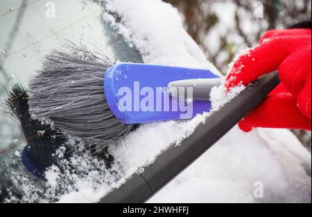 Hand der Frau mit Pinsel und entfernen Schnee von Auto und Windschutzscheibe. Winterprobleme beim Transport Stockfoto