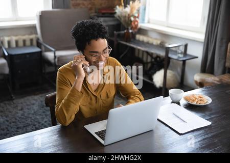 Happy Black freiberuflicher Mitarbeiter mit Brille und Fernbedienung nimmt Anruf an Stockfoto