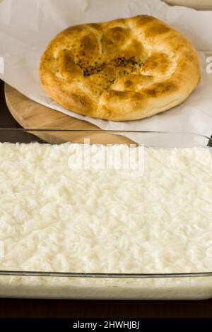 Traditionelles türkisches Ramadan Milky Dessert, Gulac in Glasbehälter auf Holztisch mit frischem runden Ramadan-Brot Stockfoto