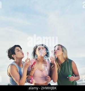 Seid einfach sprudelnd. Kurzer Schuss von drei Freunden, die am Strand Blasen blasen. Stockfoto