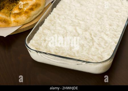 Traditionelles türkisches Ramadan Milky Dessert, Gulac in Glasbehälter auf Holztisch mit frischem runden Ramadan-Brot Stockfoto