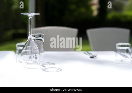 Tischset mit Gläsern über einer weißen Tischdecke im Restaurantgarten - selektiver Fokus, Kopierraum Stockfoto