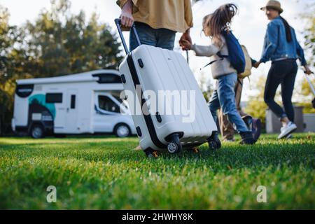 Rückansicht einer jungen Familie mit Koffern, die im Park zum Wohnwagen gehen. Stockfoto