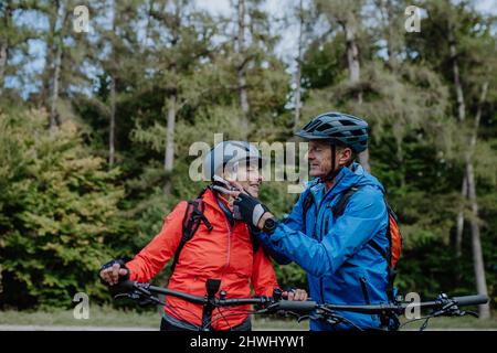Ältere Biker, die am Herbsttag im Wald im Freien Fahrradhelm aufsetzen. Stockfoto