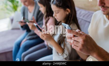 Familie mit zwei kleinen Töchtern, jeder nutzt Handy im Wohnzimmer. Stockfoto