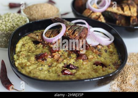 Ein Topf Zubereitung mit kodo Hirse, Mungbohnenlinse. Allgemein bekannt als kodo Hirse khichdi in Indien. Serviert mit gebratenem Makrelenfisch und Zwiebelrinne Stockfoto