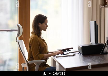 Seitenansicht junge Frau sitzt am Schreibtisch und arbeitet am pc Stockfoto