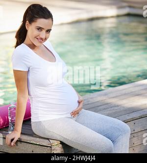 Sich nach dem Yoga total entspannt fühlen. Aufnahme einer jungen Schwangeren, die draußen mit ihrer Yogamatte sitzt. Stockfoto