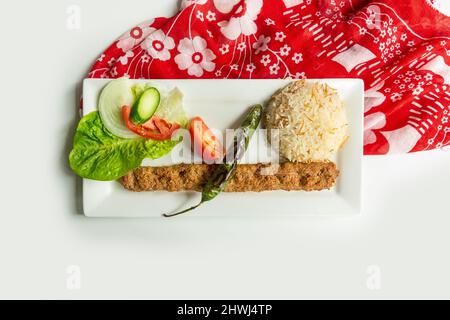 Türkischer adana Kebab mit Reis und Salat in einem Gericht isoliert auf bunten Tischtuch Draufsicht auf grauem Hintergrund Stockfoto