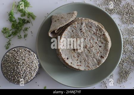 Weiches Fladenbrot aus Perlhirse-Mehl. Aufgenommen auf weißem Hintergrund zusammen mit einem Haufen Perlenhirse in einer kleinen Glasschale. Allgemein Bajr genannt Stockfoto