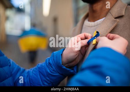 Protestorganisator verteilt ukrainische blaue und gelbe Bänder an Menschen, die gegen den Krieg in der Ukraine protestieren Stockfoto