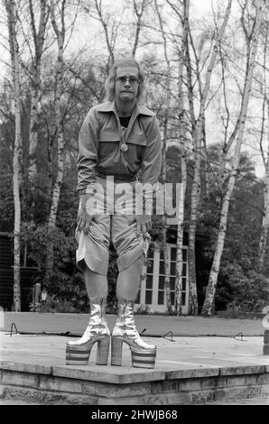 Elton John, Sänger, im Jahr 1973 zu Hause in Virginia Water abgebildet. Er spielt für die Kamera, über 3 Bilder, zieht Gesichter und zeigt seine haarigen Beine und die neuesten Platformstiefel, die 5 Platformgröße und 8 Zoll hoch sind. Sie sind silber und rot, mit seinen Initialen auf und wurden in etwa drei Tagen von Ken Todd vom Kensington Market maßgefertigt. Bild aufgenommen am 20.. März 1973 Stockfoto