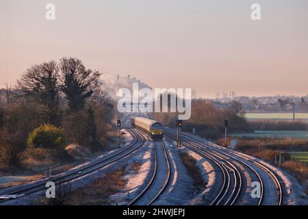 Eine Diesellokomotive der GB Railfreight der Klasse 66, die an einem frostigen Morgen mit einem Güterzug Ulleskelf passiert, liegt hinter dem Kraftwerk Ferrybridge Stockfoto
