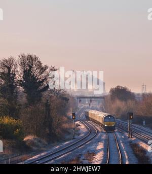 Eine Diesellokomotive der GB Railfreight der Klasse 66, die an einem frostigen Morgen mit einem Güterzug Ulleskelf passiert, liegt hinter dem Kraftwerk Ferrybridge Stockfoto