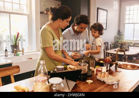 Familie beim gemeinsamen Frühstück zu Hause. Junge ethnische Familie verteilt ihr Brot mit Marmelade in der Küche. Zwei liebevolle Eltern, die etwas Qualität ausgeben Stockfoto