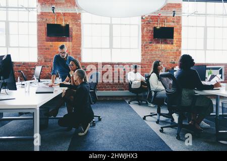 Eine Gruppe von Geschäftsleuten, die in einem kreativen, modernen Büro arbeiten. Kollegen interagieren miteinander, während sie an ihrem Schreibtisch an einem modernen Arbeitsplatz arbeiten Stockfoto