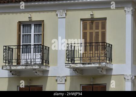 Alte neoklassizistische Hausfassade mit passenden Fenstern, hölzernen Fensterläden, ionischen Säulen und Balkonen mit schmiedeeisernem Geländer in Nafplio Griechenland. Stockfoto