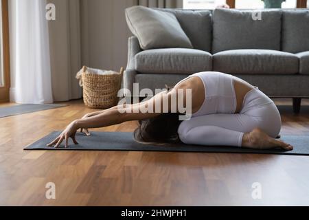 Seitenansicht Frau macht Yoga zu Hause und führt Balasana-Pose durch Stockfoto