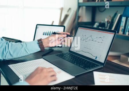 Der Geschäftsmann hält den Stift und zeigt auf den Laptop im Büro mit Dokumentbericht, Diagramm, Finanzbericht auf dem Bildschirm. Stockfoto