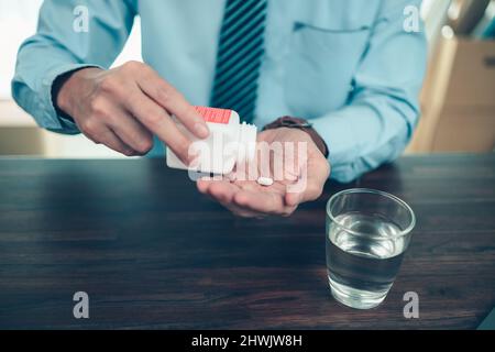 Geschäftsmann, der mit einem Glas Wasser arbeitet, nimmt Pillen in die Hand. Arbeits- und Sick-Konzept. Stockfoto