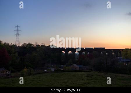 Silhouette einer Lokomotive der Baureihe 66 der GB Railfreight, die die Kapelle Milton Viaduct, Chinley, Derbyshire, mit einem Güterzug aus Steintrichtern überquert Stockfoto