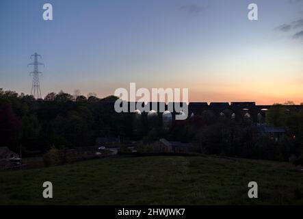 Silhouette einer Lokomotive der Baureihe 66 der GB Railfreight, die die Kapelle Milton Viaduct, Chinley, Derbyshire, mit einem Güterzug aus Steintrichtern überquert Stockfoto