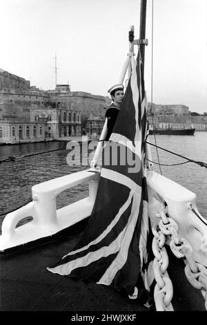 Vorbereitung auf die britische Abreise aus Malta. Der 18-jährige Radiobetreiber Brian Houston, der aus Ilford, Essex, kommt und den Union Jack bei Sonnenuntergang in H.M.S. zeigt Blake. Im Hintergrund befindet sich das Marinehauptquartier Valletta, Malta. 1972 72.-00107-005. Januar Stockfoto