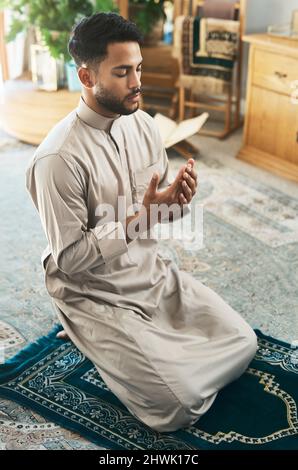 Gebet ist Hingabe. Aufnahme eines jungen muslimischen Mannes, der zu Hause in der Lounge betet. Stockfoto