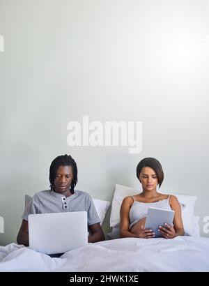 Glauben Sie nicht alles, was Sie online lesen. Aufnahme eines Paares, das im Bett sitzt, während es drahtlose Geräte verwendet. Stockfoto