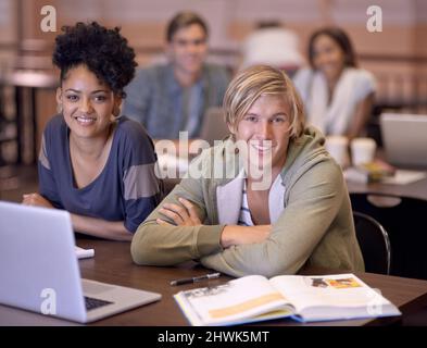 Es ist toll, einen Studienpartner zu haben. Portrait von zwei Studenten, die gemeinsam auf einem Laptop ihre Aufgaben erforschen. Stockfoto