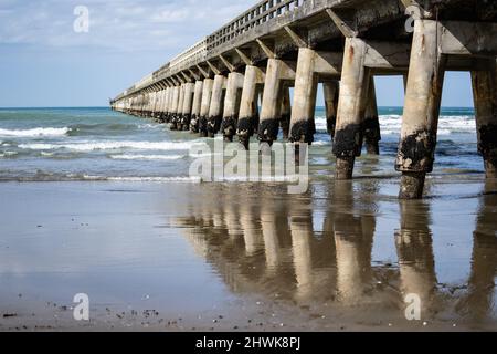 Lange, sich wiederholende Strukturmuster, Reflexion im nassen Sand und abnehmende Perspektive und Schatten der Struktur unter Tolaga Bay Wharf, Ostküste N Stockfoto