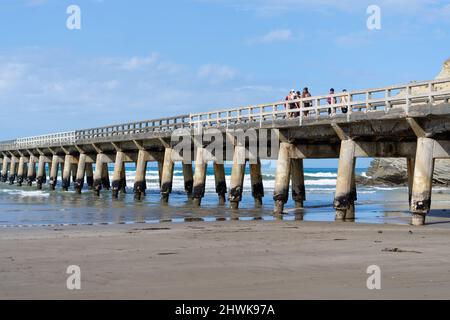 Tolaga Bay Neuseeland - Februar 5 2022; Gruppe von Menschen, die entlang der langen Werft mit sich wiederholenden strukturellen Mustern und abnehmenden Perspektiven gehen Stockfoto