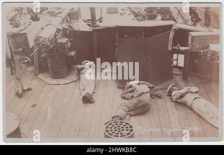 „Jack's Quiet Nap“: Fotopostkarte mit drei Matrosen der Royal Navy, die auf Deck des Schlachtschiffs HMS Jupiter liegen. Ein vierter Seemann steht neben einem Decksgewehr. Das Bild stammt aus dem frühen 20.. Jahrhundert (Ära des Ersten Weltkriegs) Stockfoto