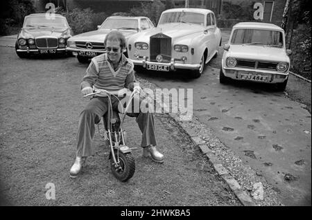 Elton John im Bild bei ihm zu Hause, sitzend auf einem kleinen Motorrad vor vier seiner Autos, darunter ein Mercedes (2. links) und ein weißer Rolls Royce (3. links).Foto vom 4.. April 1972 Stockfoto